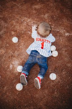 a toddler laying on the ground with baseballs all around him and his feet in the air