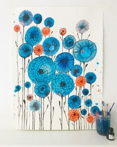 blue flowers are painted on a white wall next to a cup and vase with pencils in it