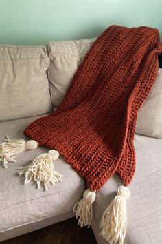 an orange crocheted blanket sitting on top of a couch next to a white pillow