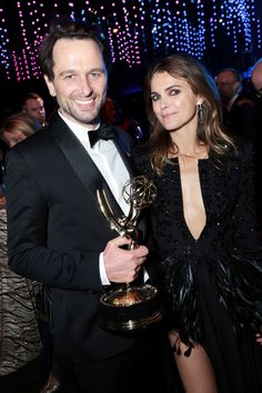 a man in a tuxedo holding an award next to a woman in a black dress