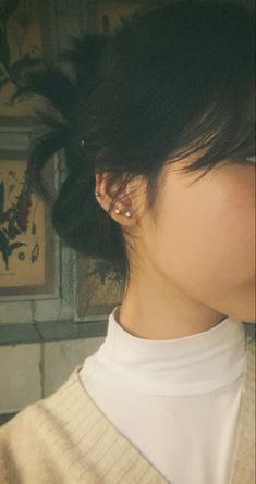 a woman with black hair wearing a white collared shirt and gold earring on her left ear