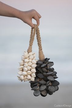 a hand is holding a pine cone with shells on it and a string attached to it