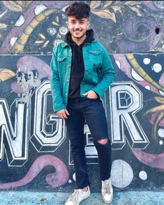 a young man standing in front of a graffiti covered wall with his hands in his pockets