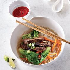 a white bowl filled with meat and veggies next to chopsticks