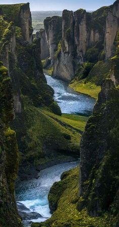 a river flowing through a lush green valley next to tall rocks and grass covered hillsides