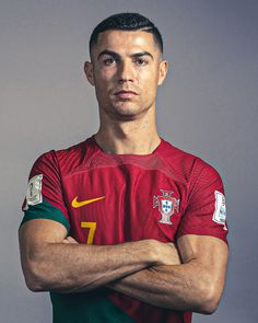 a soccer player poses for a portrait in portugal's national team uniform, with his arms crossed