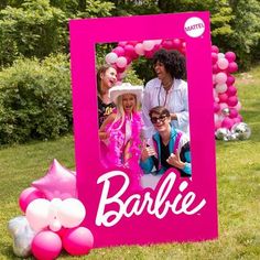 some people are posing for a picture in front of a pink frame with balloons and streamers