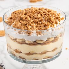 a layered dessert in a glass dish on top of a white table with cookies around it