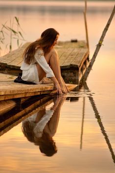 a woman sitting on the edge of a body of water next to a wooden dock