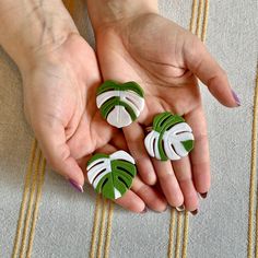 a woman's hands holding three pieces of green and white broochies with leaves on them