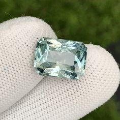 a blue diamond is sitting on someone's finger in front of some grass and bushes