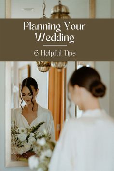 a woman standing in front of a mirror next to a flower bouquet and holding a wedding bouquet