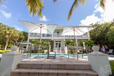 a large white house sitting next to a pool with palm trees in front of it