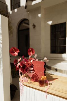 a vase filled with red flowers sitting on top of a wooden table next to a building