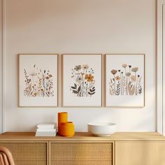 three framed pictures hang on the wall above a dresser in a white room with an orange vase