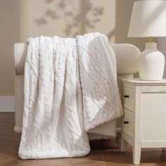 a white blanket sitting on top of a wooden floor next to a chair and lamp