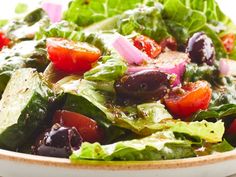 a salad with lettuce, tomatoes, olives and onions on it in a bowl