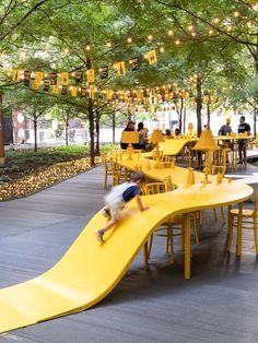 a young boy sliding down a yellow slide in the middle of an outdoor dining area