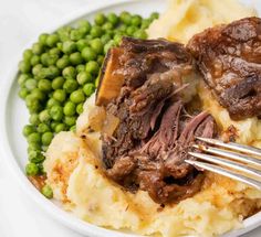 a white plate topped with meat and mashed potatoes covered in gravy next to peas