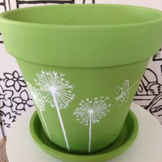 a green flower pot with white dandelions painted on the side sitting on a table