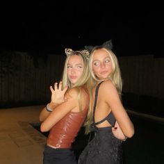 two young women standing next to each other in front of a fence at night time