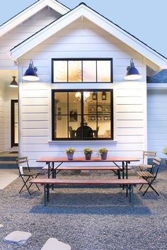 a small white house with a picnic table and benches in front of the door area