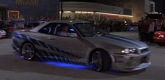 a silver car with blue stripes on it driving down the street in front of a crowd