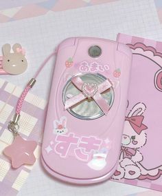 a pink hello kitty cell phone sitting on top of a table next to a keychain