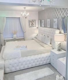 a white bed sitting in a bedroom next to a dresser and mirror with lights on it