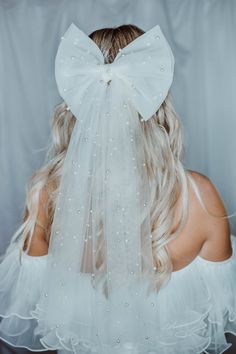 the back of a woman wearing a veil with pearls on it and a bow in her hair