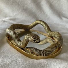 a gold snake belt is laying on a white sheet and it's curled up