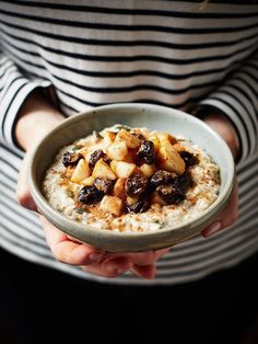 a person holding a bowl of oatmeal with raisins and nuts