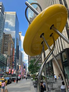 a large yellow object sitting on the side of a road next to tall buildings in a city