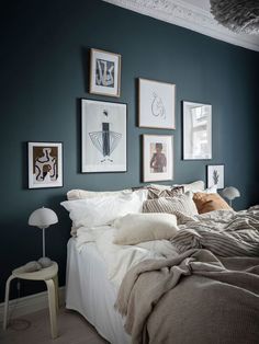 a bedroom with blue walls and pictures on the wall above the bed, along with white linens