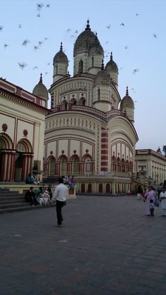 people are walking around in front of a large building with many spires and domes