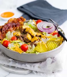 a salad with bacon, lettuce, tomatoes and onions in a white bowl