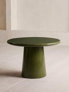 a round green table sitting on top of a white floor next to a vase and potted plant