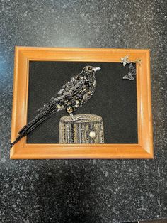 a black bird sitting on top of a piece of wood next to a wooden frame