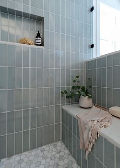 a white bath tub sitting under a window next to a tiled bathroom floor and wall