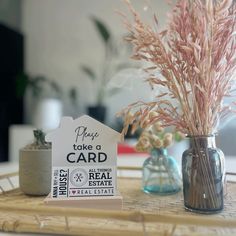 there is a small house shaped card on the table next to two vases with flowers in them