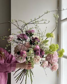 a woman holding a bouquet of flowers in front of a window with white and pink colors