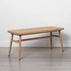 a wooden bench sitting on top of a hard wood floor next to a white wall