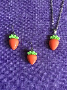 two necklaces with carrots on them sitting next to each other in front of a purple background