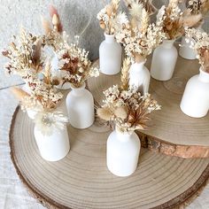 white vases filled with dried flowers sitting on top of a tree stump in front of a wall