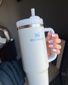 a woman holding a white coffee cup with the word stanley on it and a silver lid