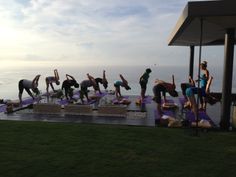 a group of people doing yoga on top of a wooden platform near the water with their arms in the air