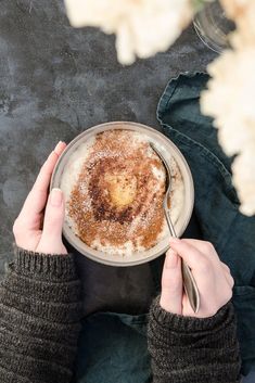 two hands holding a bowl of food with powdered sugar on top and spoon in the other hand