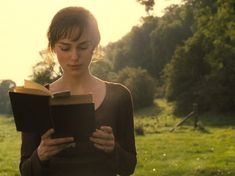 a woman is reading a book in the grass with trees in the backgroud