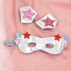 two white masks with red and blue stars on them sitting on a pink cloth background