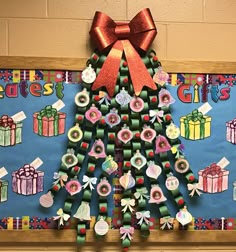 a christmas tree made out of rolled up paper and ribbon on a bulletin board with presents tied to it